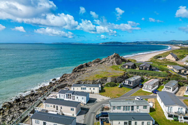 Coastal holiday park with sea view, caravans, and rocky shoreline under blue sky.