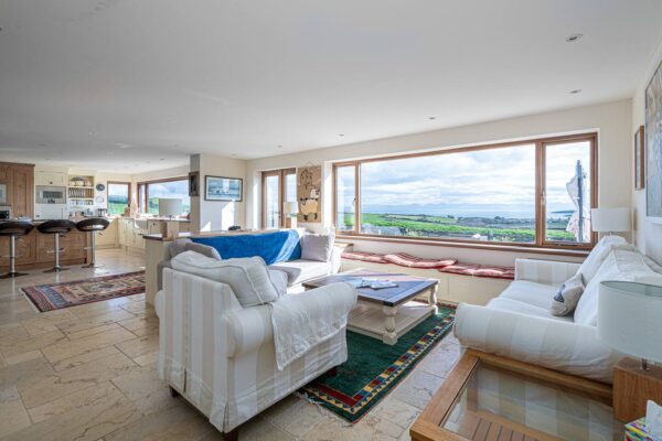 Spacious living room with sea view, cozy seating, and modern kitchen in bright, airy open-plan home.